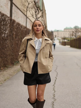 a lady wears a cropped trench coat with striped sweater and black shorts